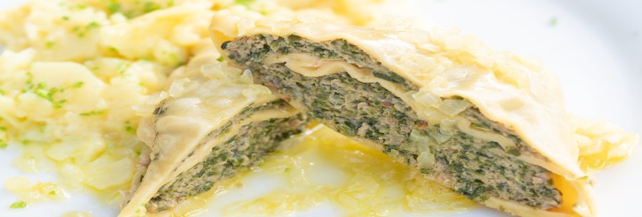 Nahaufnahme von Maultaschen mit einer Füllung aus Fleisch und Kräutern, serviert mit Kartoffelsalat auf einem weißen Teller., © Herr Kächele - Schwäbisches für Schleckige GmbH