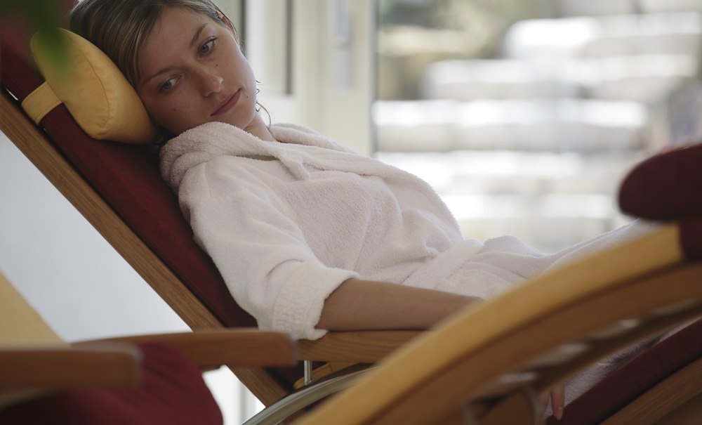 A woman in a white bathrobe is relaxing on a lounge chair in a bright room with stairs in the background., © Badhotel Restaurant Stauferland A woman in a white bathrobe is relaxing on a lounge chair in a bright room with stairs in the background., © Badhotel Restaurant Stauferland