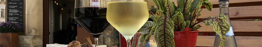 A table with a glass of red and white wine, bread, a small dish and a plant in front of the 'Speisekammer West' restaurant., &copy; Speisekammer West