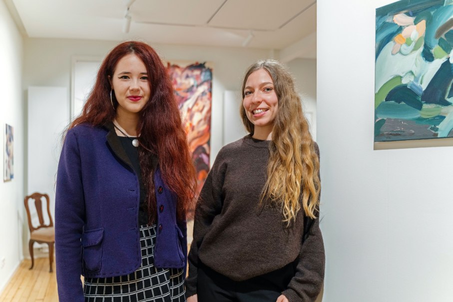 Zwei Frauen in einer Kunstgalerie, umgeben von Gem&auml;lden. Sie l&auml;cheln in die Kamera und stehen vor einer wei&szlig;en Wand mit Kunstwerken., &copy; Dominique Brewing