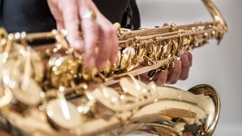 Nahaufnahme eines goldenen Saxophons, das von einer Person gehalten und gespielt wird. Die Hände sind auf den Tasten positioniert., © Jens Volle Nahaufnahme eines goldenen Saxophons, das von einer Person gehalten und gespielt wird. Die Hände sind auf den Tasten positioniert., © Jens Volle