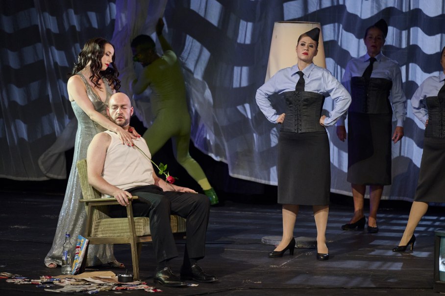 Theaterszene mit einer Frau in einem glitzernden Kleid, die einem sitzenden Mann eine Rose reicht. Weitere Personen in Uniformen stehen im Hintergrund., &copy; Martin Sigmund