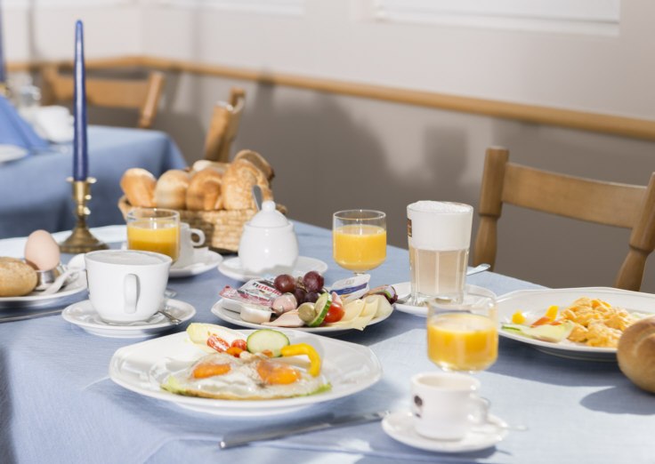 Ein reich gedeckter Frühstückstisch mit Brötchen, Eiern, Orangensaft, Kaffee und verschiedenen Beilagen auf blauer Tischdecke., © Hotel Adler Waiblingen Ein reich gedeckter Frühstückstisch mit Brötchen, Eiern, Orangensaft, Kaffee und verschiedenen Beilagen auf blauer Tischdecke., © Hotel Adler Waiblingen