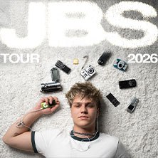Ein junger Mann liegt auf einem Teppich, umgeben von Kameras und Geräten. Oben steht 'JBS Tour 2026'., © links im Bild Ein junger Mann liegt auf einem Teppich, umgeben von Kameras und Geräten. Oben steht 'JBS Tour 2026'., © links im Bild