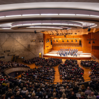 A large concert hall with a modern design, filled with spectators. An orchestra plays on the stage. The architecture is impressive., © Holger Schneider A large concert hall with a modern design, filled with spectators. An orchestra plays on the stage. The architecture is impressive., © Holger Schneider