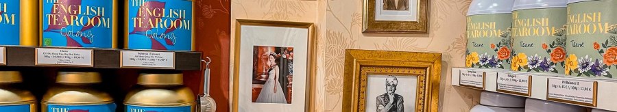 Regale mit Teedosen von 'The English Tearoom' und gerahmte Fotos an einer dekorativen Wand., &copy; Tea Room, Stuttgart