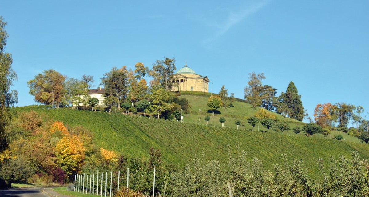 Die Grabkapelle Württemberg thront auf einem Hügel, umgeben von Bäumen und Weinbergen, unter einem klaren blauen Himmel., © Stuttgart-Marketing GmbH Die Grabkapelle Württemberg thront auf einem Hügel, umgeben von Bäumen und Weinbergen, unter einem klaren blauen Himmel., © Stuttgart-Marketing GmbH