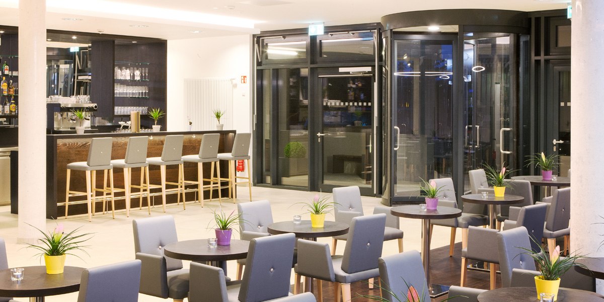 Moderne Bar mit Theke, Barhockern und kleinen Tischen. Pflanzen in bunten Töpfen dekorieren den Raum. Große Glastüren im Hintergrund., © Star Inn Stuttgart Airport-Messe Moderne Bar mit Theke, Barhockern und kleinen Tischen. Pflanzen in bunten Töpfen dekorieren den Raum. Große Glastüren im Hintergrund., © Star Inn Stuttgart Airport-Messe