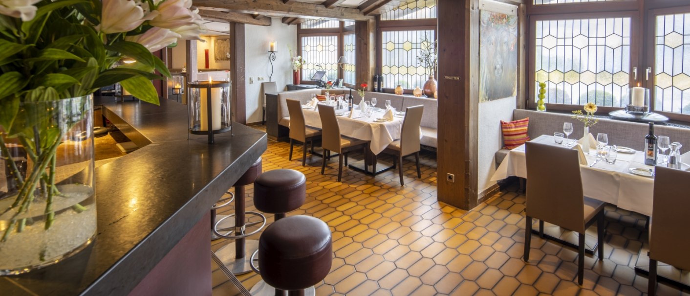 Ein gemütliches Restaurant mit Holzbalkendecke, gedeckten Tischen und großen Fenstern. Blumen und Kerzen sorgen für eine einladende Atmosphäre., © Hotel Gloria GmbH Ein gemütliches Restaurant mit Holzbalkendecke, gedeckten Tischen und großen Fenstern. Blumen und Kerzen sorgen für eine einladende Atmosphäre., © Hotel Gloria GmbH