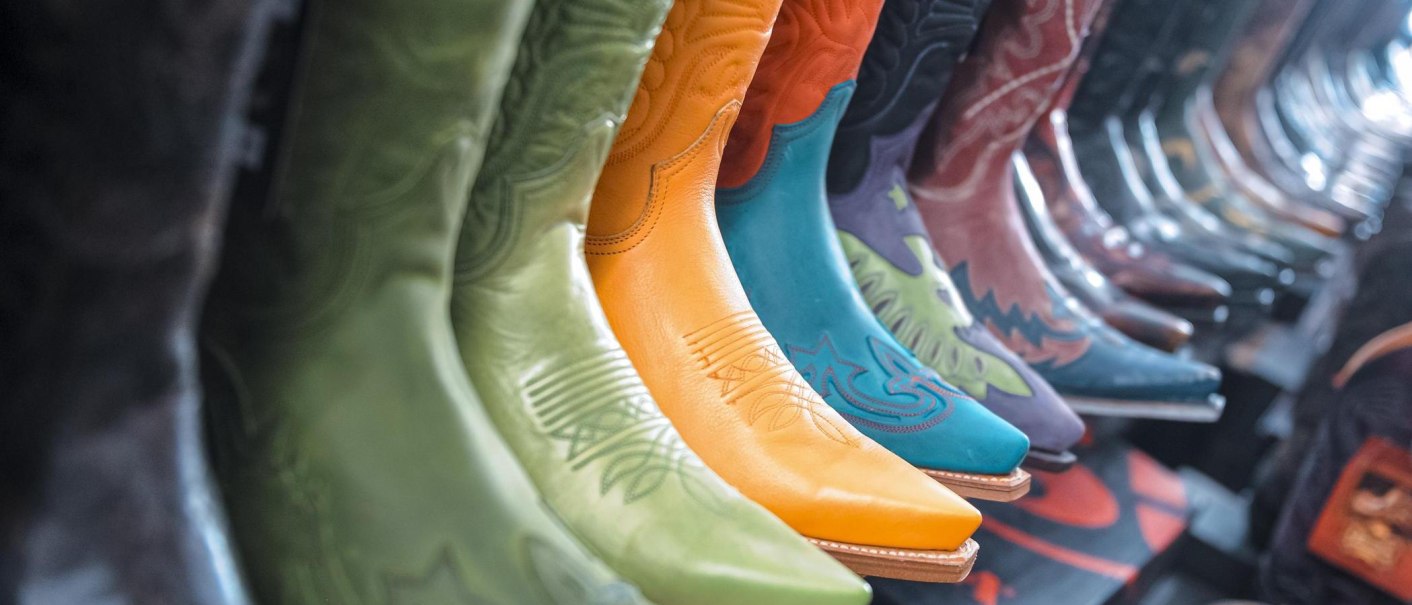Eine Reihe bunter Cowboy-Stiefel in verschiedenen Farben und Mustern, darunter gr&uuml;n, orange und blau, in einem Gesch&auml;ft ausgestellt., &copy; DBoots by Boots, Stuttgart