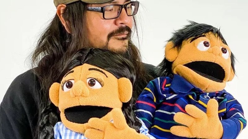 Ein Mann mit Brille und Bart hält zwei Puppen, eine in einem blauen Hemd und eine in einem karierten Hemd, vor einem weißen Hintergrund., © Pete Sands Ein Mann mit Brille und Bart hält zwei Puppen, eine in einem blauen Hemd und eine in einem karierten Hemd, vor einem weißen Hintergrund., © Pete Sands