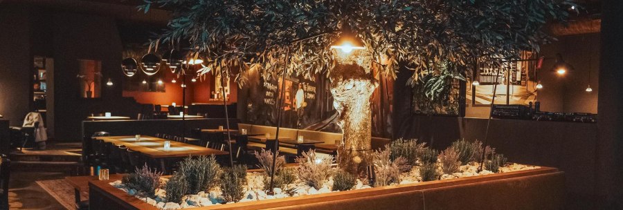 A warmly lit restaurant interior featuring a large artificial tree as the centerpiece and modern seating areas., &copy; L'Artista, Stuttgart