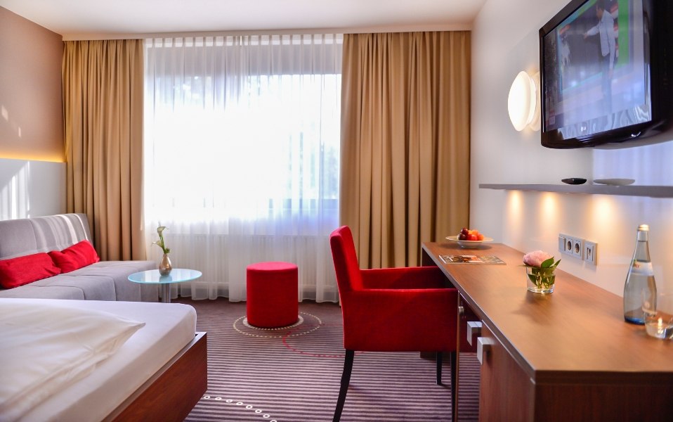 Modern hotel room with double bed, sofa, desk, TV and large windows. Red accents and subtle lighting create a cozy atmosphere., © Hotel Fuchsen Modern hotel room with double bed, sofa, desk, TV and large windows. Red accents and subtle lighting create a cozy atmosphere., © Hotel Fuchsen