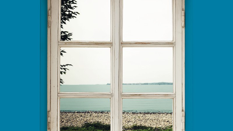 A window in a blue wall looks out onto a beach and the sea. The sky is cloudy, and a tree is visible in the distance., © Theater der Altstadt A window in a blue wall looks out onto a beach and the sea. The sky is cloudy, and a tree is visible in the distance., © Theater der Altstadt