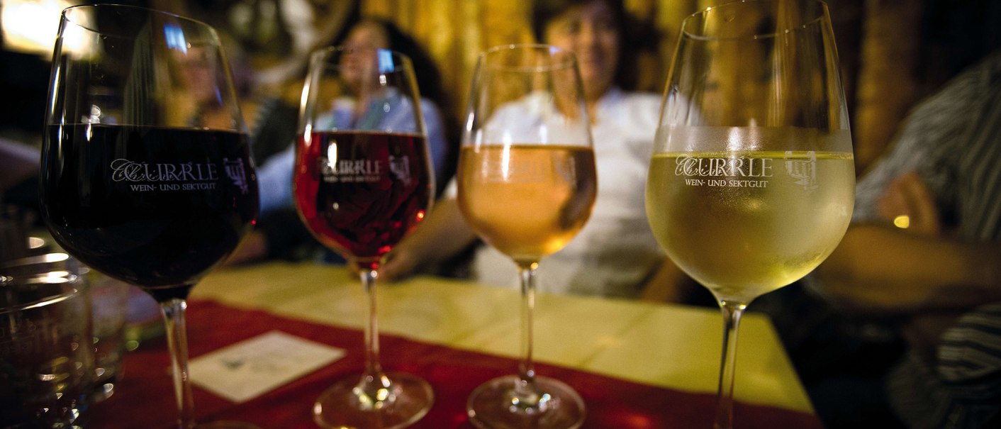 Four wine glasses with different types of wine stand on a table. People can be seen out of focus in the background., © Stuttgart-Marketing GmbH Four wine glasses with different types of wine stand on a table. People can be seen out of focus in the background., © Stuttgart-Marketing GmbH