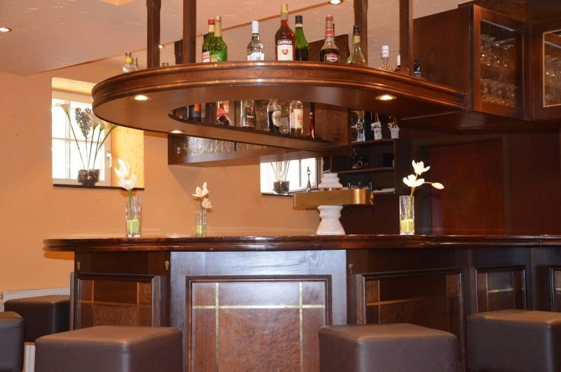 Elegant hotel bar with dark wooden counter, bottles on the shelf and decorative flower vases. Stools around the bar., &copy; TOMAS