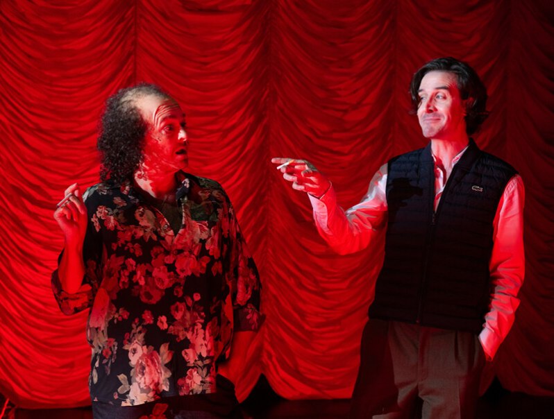 Zwei Männer stehen vor einem roten Vorhang. Der linke trägt ein Blumenhemd, der rechte eine Weste. Beide gestikulieren lebhaft., © Württembergische Staatstheater Stuttgart Zwei Männer stehen vor einem roten Vorhang. Der linke trägt ein Blumenhemd, der rechte eine Weste. Beide gestikulieren lebhaft., © Württembergische Staatstheater Stuttgart