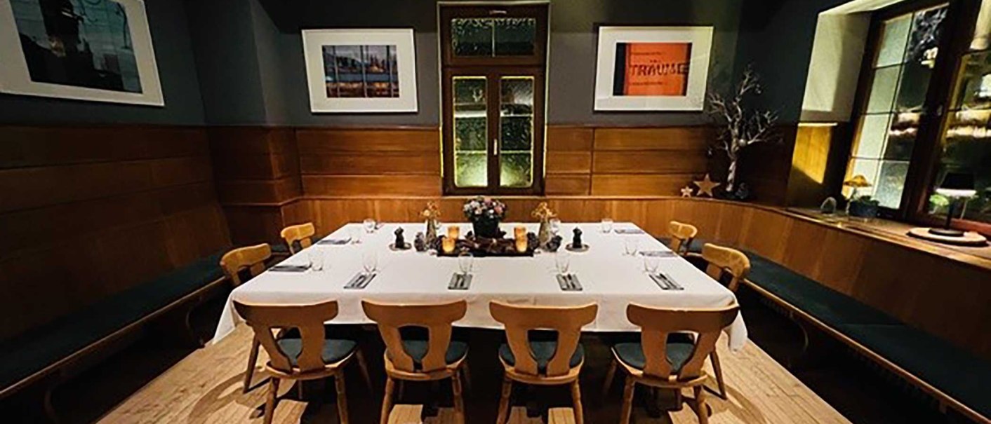 An elegant room with wooden walls, a large table with white tablecloths and chairs. Works of art hang on the walls and the window has a decorative design., © Zumbecher An elegant room with wooden walls, a large table with white tablecloths and chairs. Works of art hang on the walls and the window has a decorative design., © Zumbecher