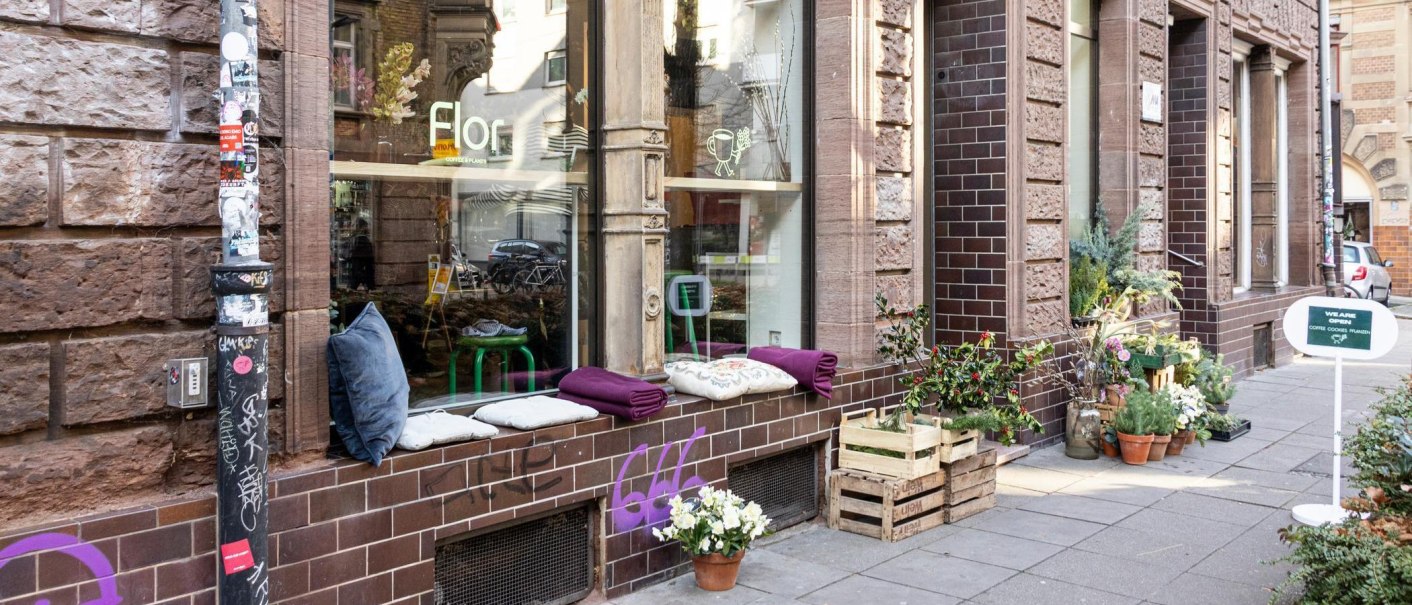A cozy caf&eacute; with plants and cushions on the windowsill. A sign advertises coffee and cookies. The fa&ccedil;ade is made of brown bricks., &copy; Stuttgart-Marketing GmbH, Sarah Schmid