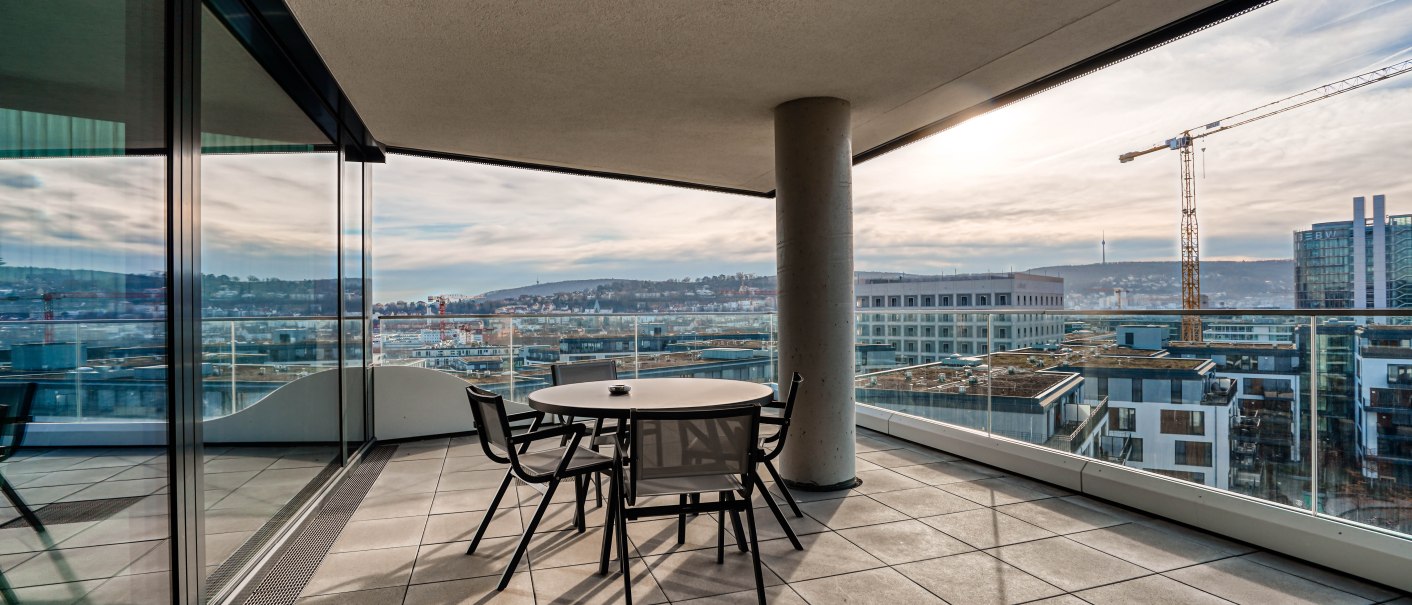 Moderner Balkon mit Tisch und Stühlen, bietet einen weiten Blick über die Stadt und einen Baukran in der Ferne., © CLOUD N°7 APARTMENTS GmbH Moderner Balkon mit Tisch und Stühlen, bietet einen weiten Blick über die Stadt und einen Baukran in der Ferne., © CLOUD N°7 APARTMENTS GmbH