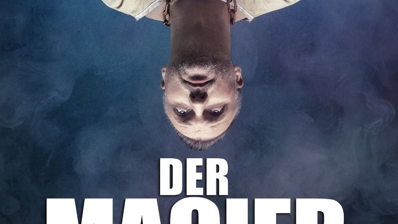 Ein kopfüber hängender Mann in Zwangsjacke vor nebligem Hintergrund. Text: 'Der Magier Live' in großen Buchstaben., © Theaterhaus Stuttgart e.V. Ein kopfüber hängender Mann in Zwangsjacke vor nebligem Hintergrund. Text: 'Der Magier Live' in großen Buchstaben., © Theaterhaus Stuttgart e.V.