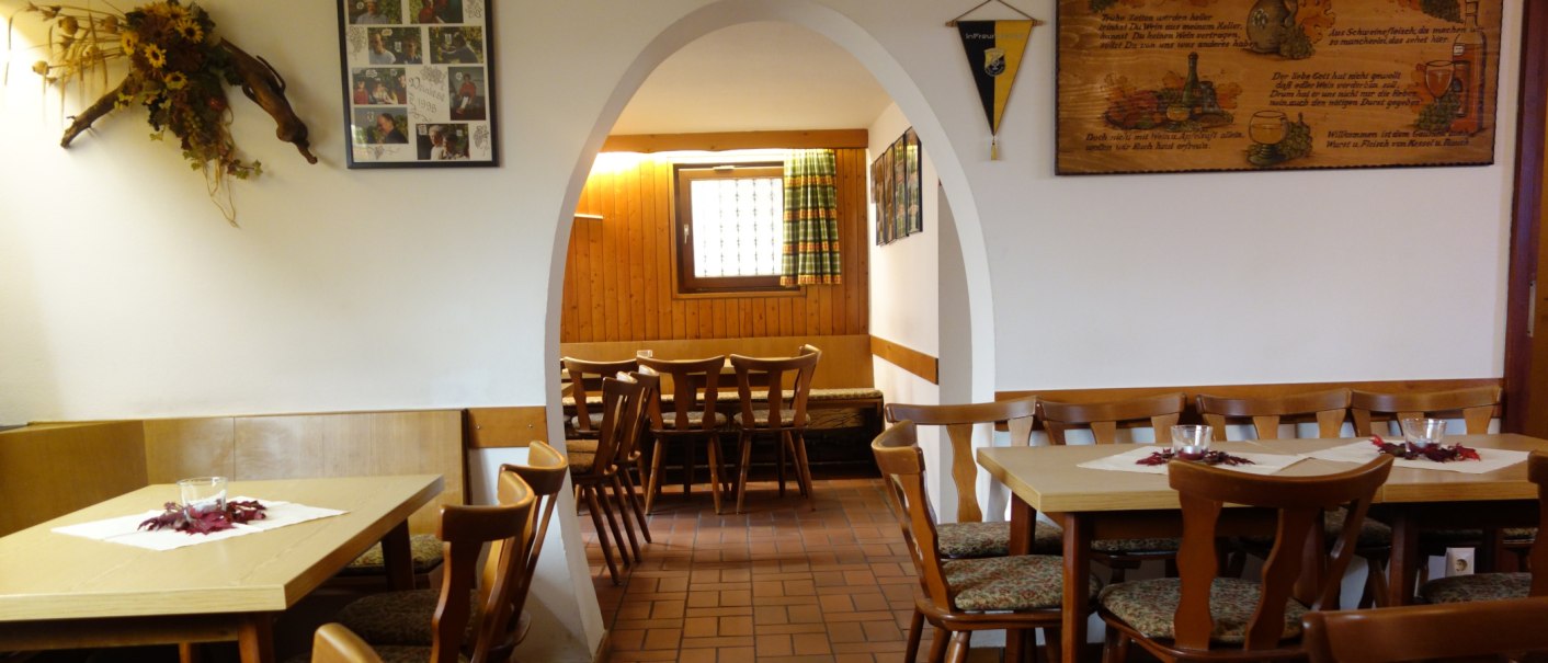 A cozy restaurant with wooden tables and chairs, decorated with pictures and flowers. An arch leads into another room., &copy; Besenwirtschaft Familie Nerz