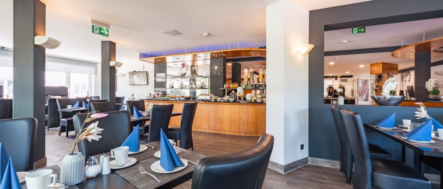 Modern restaurant with elegant black chairs, laid tables and a buffet area. Subtle lighting and decorations create an inviting atmosphere., © Plaza INN Stuttgart-Filderstadt Modern restaurant with elegant black chairs, laid tables and a buffet area. Subtle lighting and decorations create an inviting atmosphere., © Plaza INN Stuttgart-Filderstadt