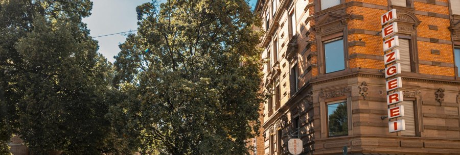 A street corner with a butcher's shop and a café on Bismarckplatz. People are sitting outside under trees, bicycles are parked., © SMG Stuttgart Marketing GmbH - Sarah Schmid