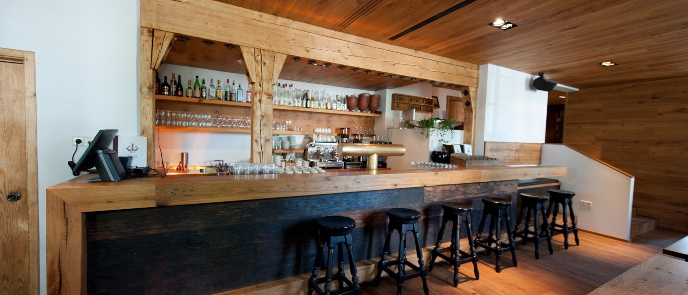 Eine gemütliche Bar mit Holzeinrichtung, Barhockern und Regalen voller Flaschen und Gläser. Die Theke ist aus dunklem Holz., © Ruthenberg&Schlatter GbR Eine gemütliche Bar mit Holzeinrichtung, Barhockern und Regalen voller Flaschen und Gläser. Die Theke ist aus dunklem Holz., © Ruthenberg&Schlatter GbR