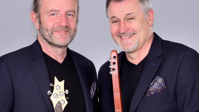 Zwei Männer in dunklen Anzügen lächeln in die Kamera. Einer hält eine Gitarre, der andere ein Holzblasinstrument., © Renitenztheater Stuttgart e.V. Zwei Männer in dunklen Anzügen lächeln in die Kamera. Einer hält eine Gitarre, der andere ein Holzblasinstrument., © Renitenztheater Stuttgart e.V.