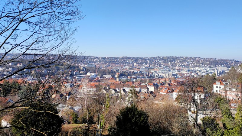 Stadtansicht mit roten D&auml;chern unter klarem, blauem Himmel. Im Vordergrund B&auml;ume und ein Holzzaun., &copy; SMG