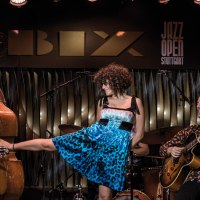 Eine Band spielt im BIX Jazzclub. Ein Gitarrist, ein Kontrabassist und eine Sängerin in blauem Kleid sind zu sehen. "Jazz Open Stuttgart" im Hintergrund., © Peter Steinheisser