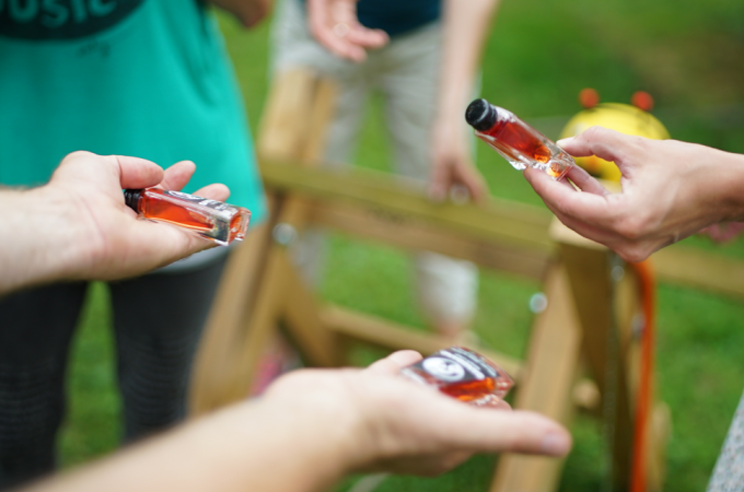 Mehrere Personen halten kleine Flaschen mit roter Fl&uuml;ssigkeit. Im Hintergrund ist ein Holzbock zu sehen., &copy; Cool-Tours StattReisen