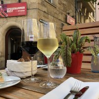 A table with a glass of red and white wine, bread, a small dish and a plant in front of the 'Speisekammer West' restaurant., &copy; Speisekammer West