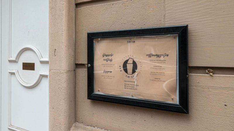 Schild der TinTin Bar mit Öffnungszeiten und Preisen an einer Wand neben einer weißen Tür., © SMG, Sarah Schmid