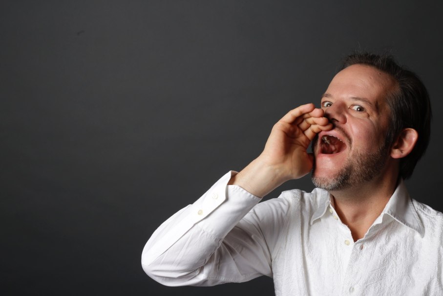 Ein Mann in einem wei&szlig;en Hemd ruft mit der Hand an seinem Mund vor einem grauen Hintergrund. Er hat einen Bart und wirkt ausdrucksstark., &copy; Pablo Fernandez
