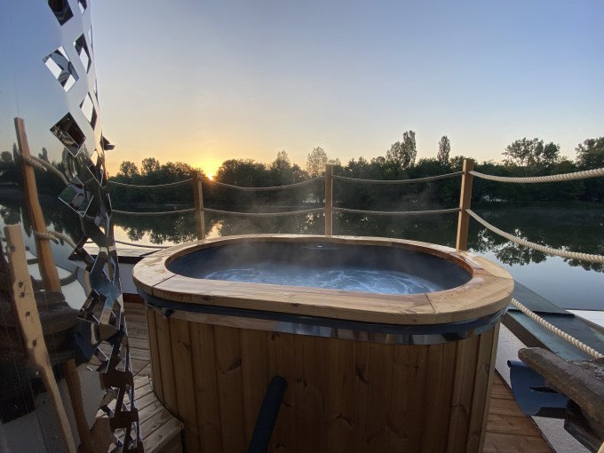 Whirlpool auf Terrasse am Fluss bei Sonnenuntergang, umgeben von Bäumen und Seilen., © Cool-Tours StattReisen Whirlpool auf Terrasse am Fluss bei Sonnenuntergang, umgeben von Bäumen und Seilen., © Cool-Tours StattReisen