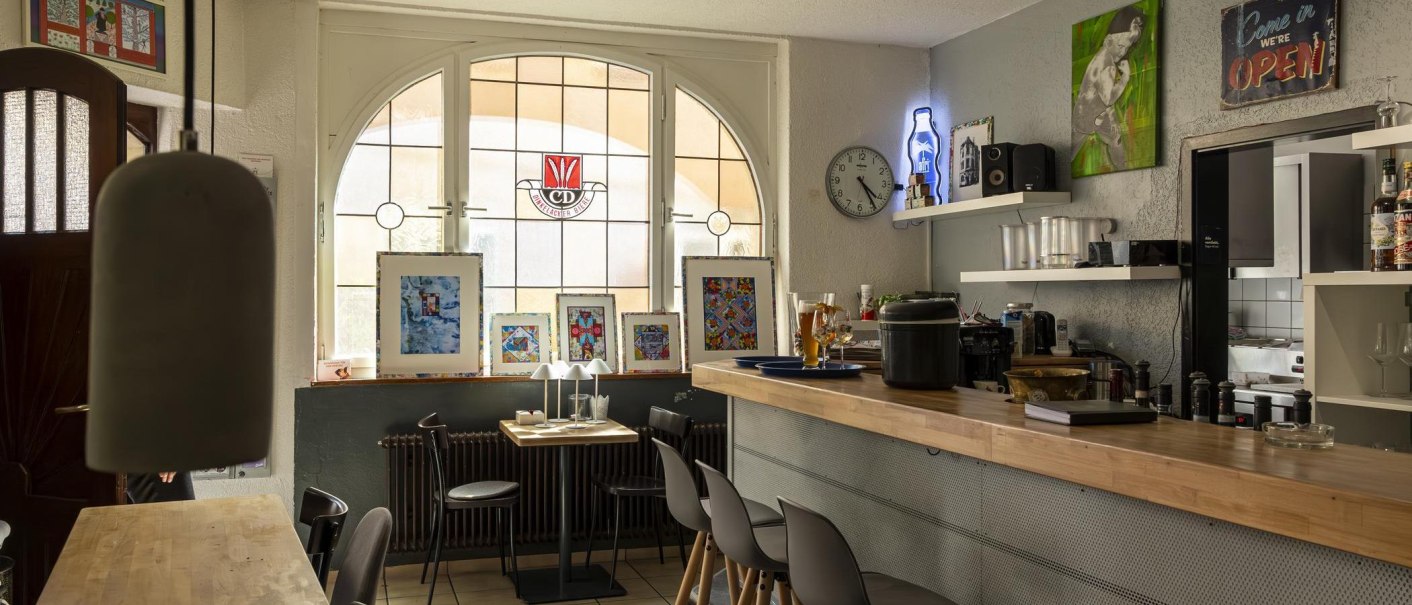 Gem&uuml;tliches Caf&eacute; mit Holztresen, Kunstwerken an den W&auml;nden und einem gro&szlig;en Fenster. Eine Uhr und Dekorationen schm&uuml;cken den Raum., &copy; SMG, Sarah Schmid