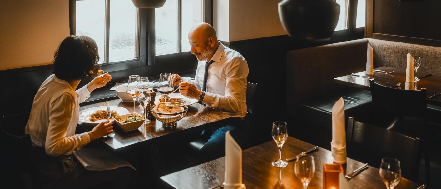 Zwei Personen essen in einem stilvoll eingerichteten Restaurant. Auf dem Tisch stehen Weingläser und Teller mit Speisen., © SMG, Alwin Maigler