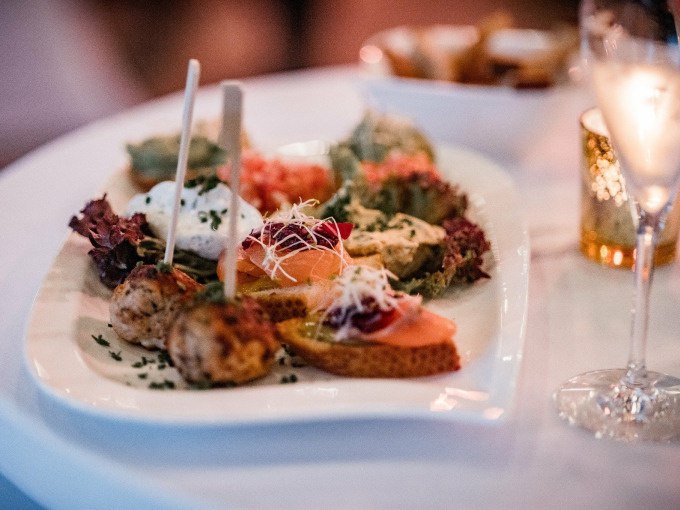 Ein Teller mit verschiedenen Vorspeisen, darunter Brot mit Lachs und Fleischb&auml;llchen, auf einem Tisch mit einem Glas Sekt., &copy; Cool-Tours StattReisen
