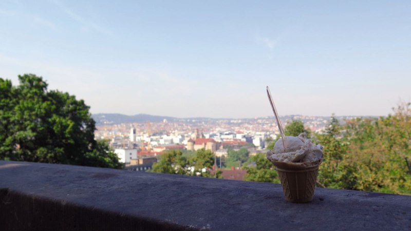 Ein Eisbecher steht auf einer Mauer mit Blick auf die Stadt Stuttgart vom Eugensplatz aus. Im Hintergrund sind Bäume und Gebäude zu sehen., © Stuttgart-Marketing GmbH