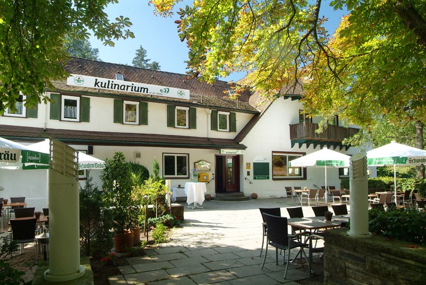 A restaurant with a patio, surrounded by trees. Tables and chairs are set up under umbrellas. The building has green shutters., &copy; Kulinarium an der Glems