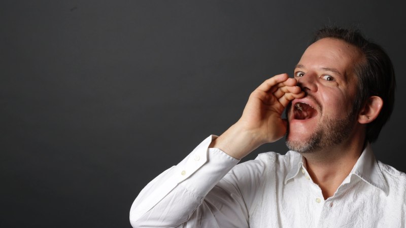 Ein Mann in einem weißen Hemd ruft mit der Hand an seinem Mund vor einem grauen Hintergrund. Er hat einen Bart und wirkt ausdrucksstark., © Pablo Fernandez Ein Mann in einem weißen Hemd ruft mit der Hand an seinem Mund vor einem grauen Hintergrund. Er hat einen Bart und wirkt ausdrucksstark., © Pablo Fernandez