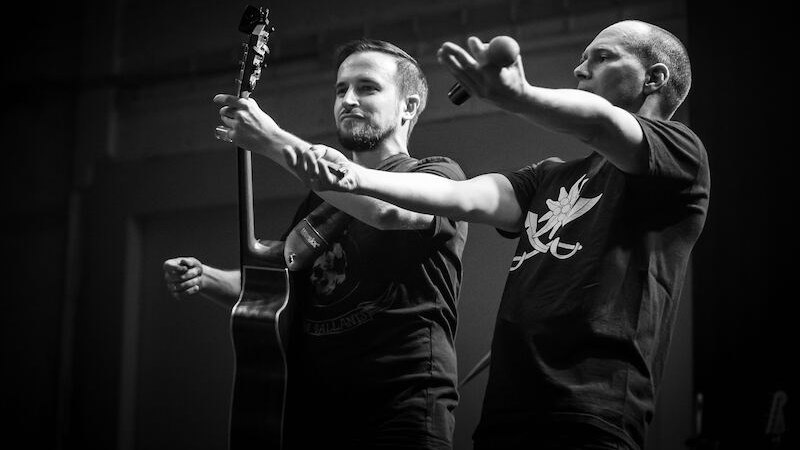 Two musicians on stage, one holding a guitar, the other a microphone. Both are wearing black T-shirts. Black and white photograph., &copy; Rosenau Kultur e.V.