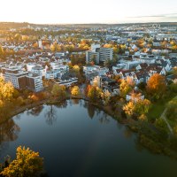 Aerial view of the Klostersee in Sindelfingen, surrounded by autumnal trees and residential buildings at sunset., © Christoph Partsch Aerial view of the Klostersee in Sindelfingen, surrounded by autumnal trees and residential buildings at sunset., © Christoph Partsch
