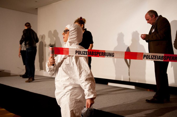 Person in protective suit in front of police cordon, other people in the background on a stage. Scene looks like a detective story in a museum., &copy; Landesmuseum W&uuml;rttemberg