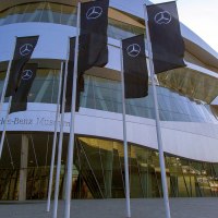 The Mercedes-Benz Museum with its modern architecture and several flags in the foreground. The sky is clear and blue., &copy; SMG, Achim Mende