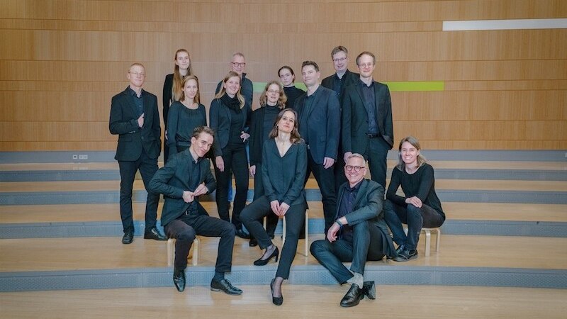 Eine Gruppe von 14 Personen in schwarzer Kleidung posiert auf einer Bühne mit Holzverkleidung im Hintergrund., © Katholische Gesamtkirchengemeinde Stuttgart-Mitte, KdöR