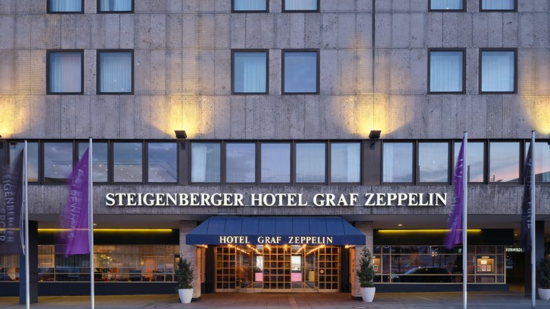 Außenansicht des Steigenberger Hotel Graf Zeppelin mit beleuchtetem Eingang und Fahnen., © Steigenberger Graf Zeppelin