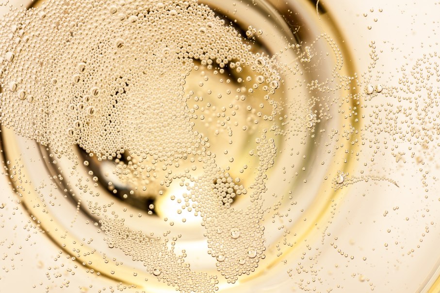 Nahaufnahme von vielen kleinen Champagnerblasen, die in einem Glas aufsteigen und ein schimmerndes Muster bilden., © unpict.com Nahaufnahme von vielen kleinen Champagnerblasen, die in einem Glas aufsteigen und ein schimmerndes Muster bilden., © unpict.com